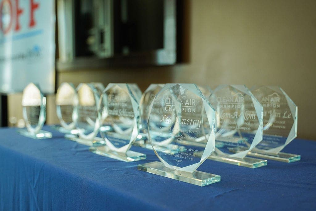 A row of glass Clean Air Champion award trophies engraved with winners’ names on a blue tablecloth