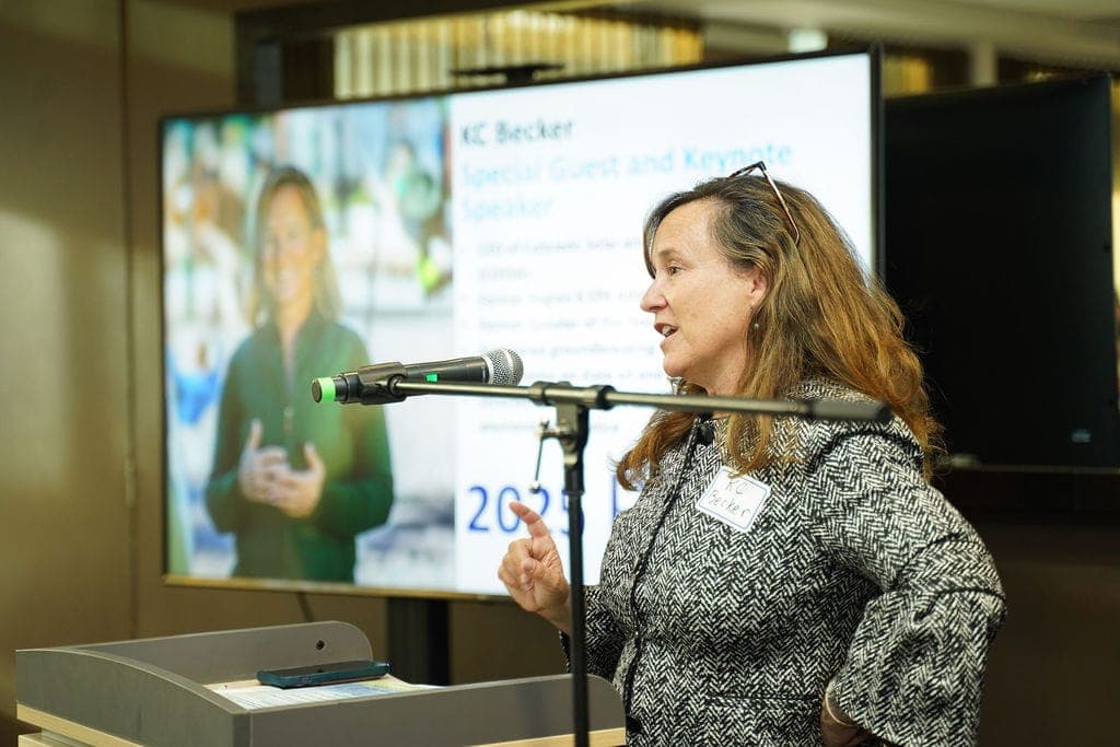 KC Becker, special guest and keynote speaker, speaks at a microphone at the Clean Air Champions awards