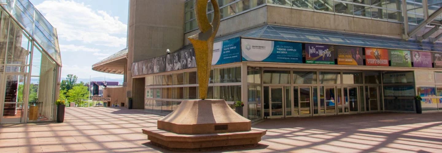 The outdoor plaza of the Helen Bonfils Theatre Complex in Denver, with a gold sculpture, box office windows and show posters