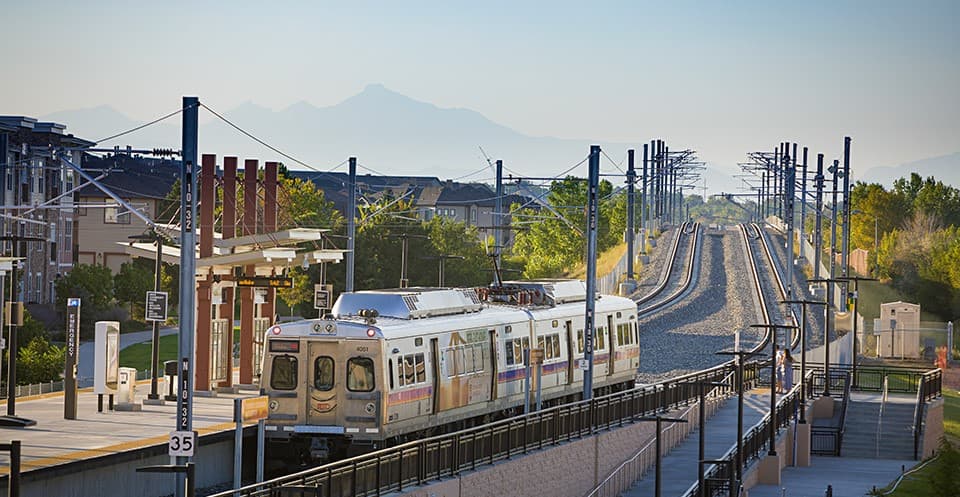 An RTD commuter rail train at an elevated station in golden evening light, with Longs Peak in the distance